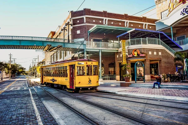 Vintage yellow streetcar on brick-paved tracks in Ybor City, Tampa Bay, Florida, with historic brick buildings nearby.